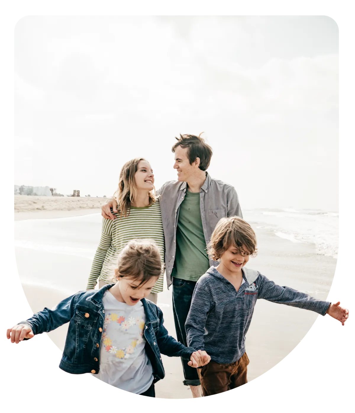 Parents looking at each other happily along a beach while their two children hold hands and walk a few steps in front of them laughing