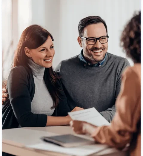 A smiling couple reviewing life insurance documents with an advisor during a consultation.